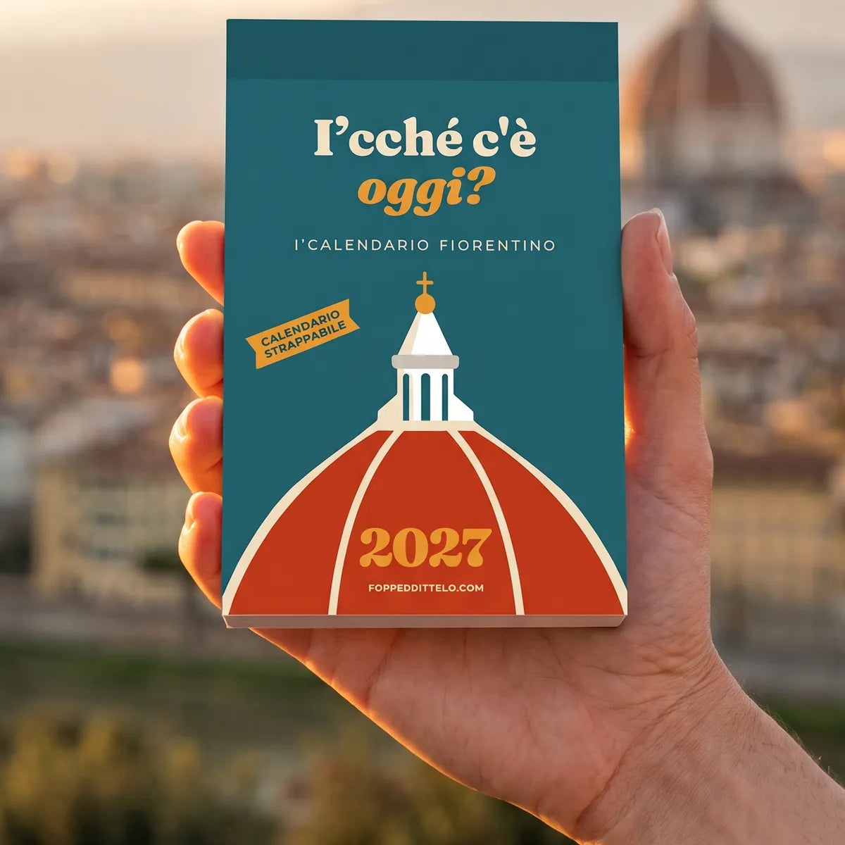 Una mano tiene il calendario «I'cché c'è oggi?» davanti al panorama di Firenze al tramonto