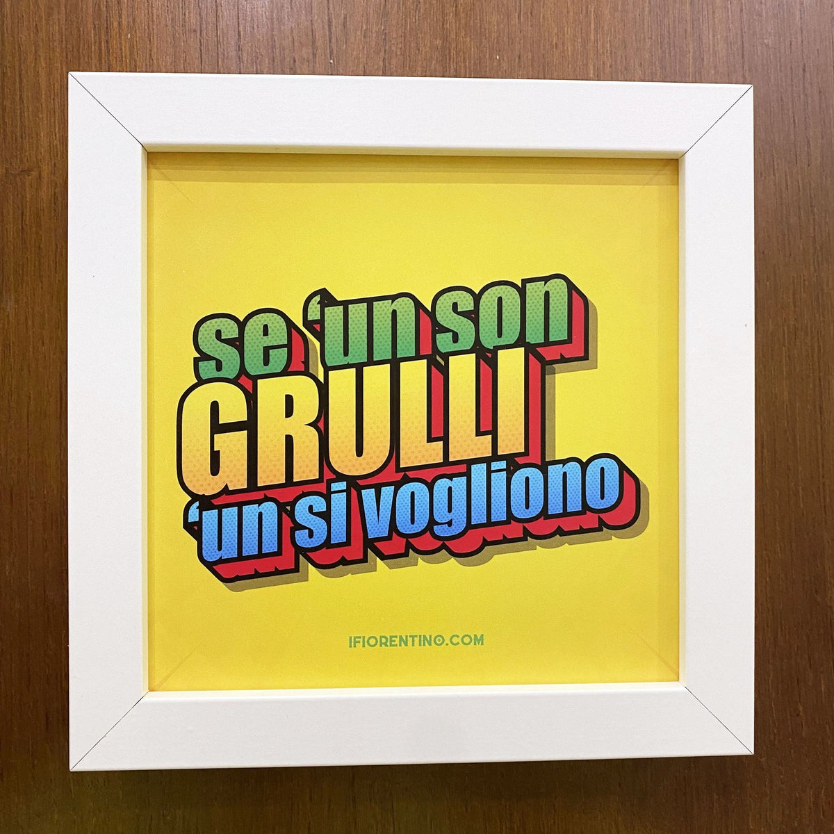 Stampa gialla «Se 'un son grulli 'un si vogliono» in cornice bianca su parete di legno